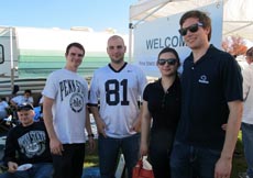 Four students posing in front of the welcome sign at the football tailgate